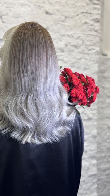 بالیاژ از قهوه‌ای روشن به نقره‌ای یخی روی موی بلند با موج نرم، همراه با دسته‌گل رز قرمز