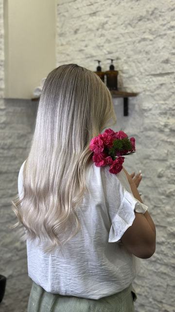 بالیاژ بلوند خاکستری روی موی بلند و موج‌دار با گل صورتی در مو